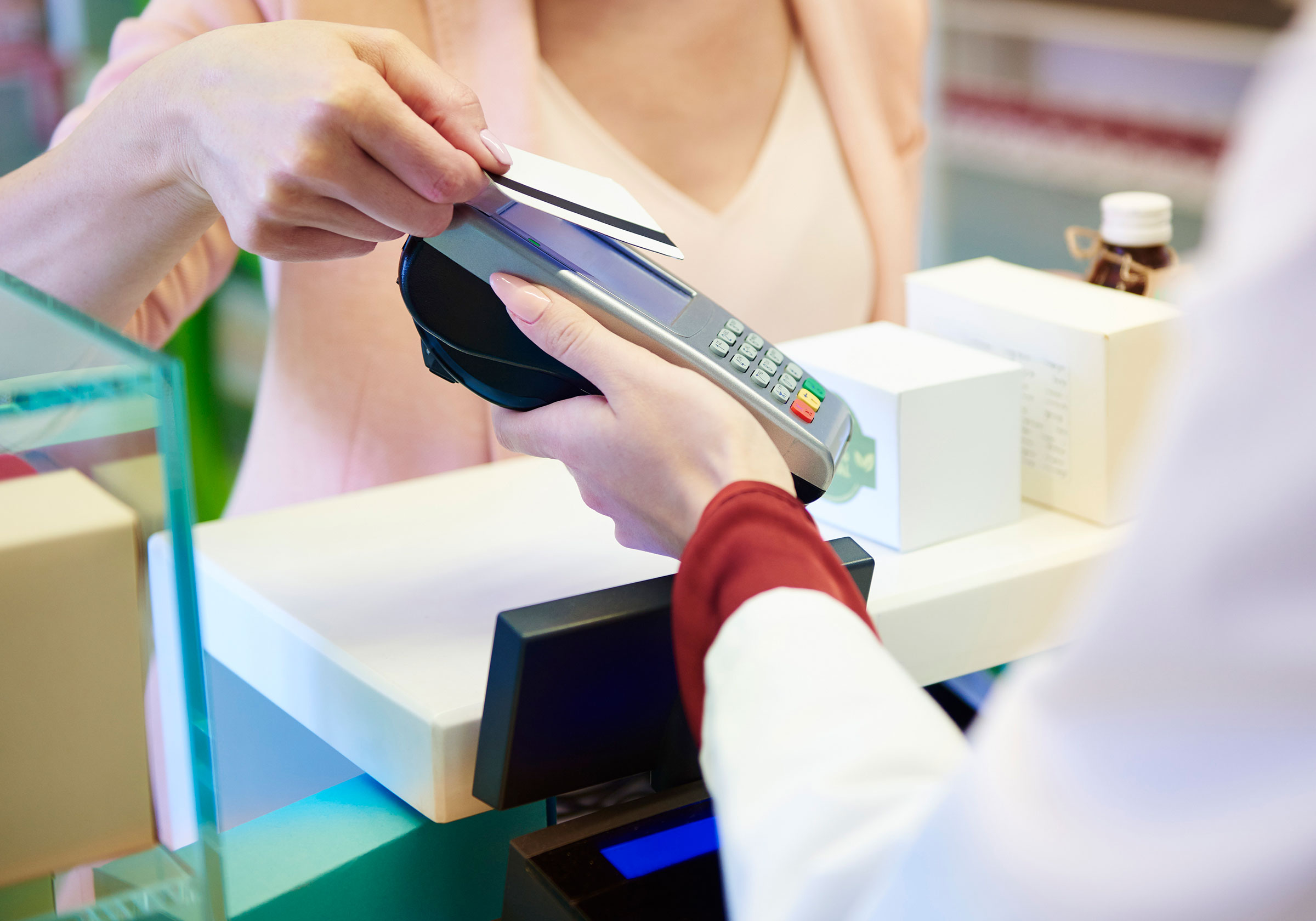 Hand hält Karte an ein Bezahlterminal an der Kasse, andere Person gegenüber